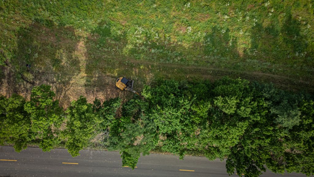 Drone view of an excavator with a forestry mulching attachment as an operator clears the overgrown field edges.