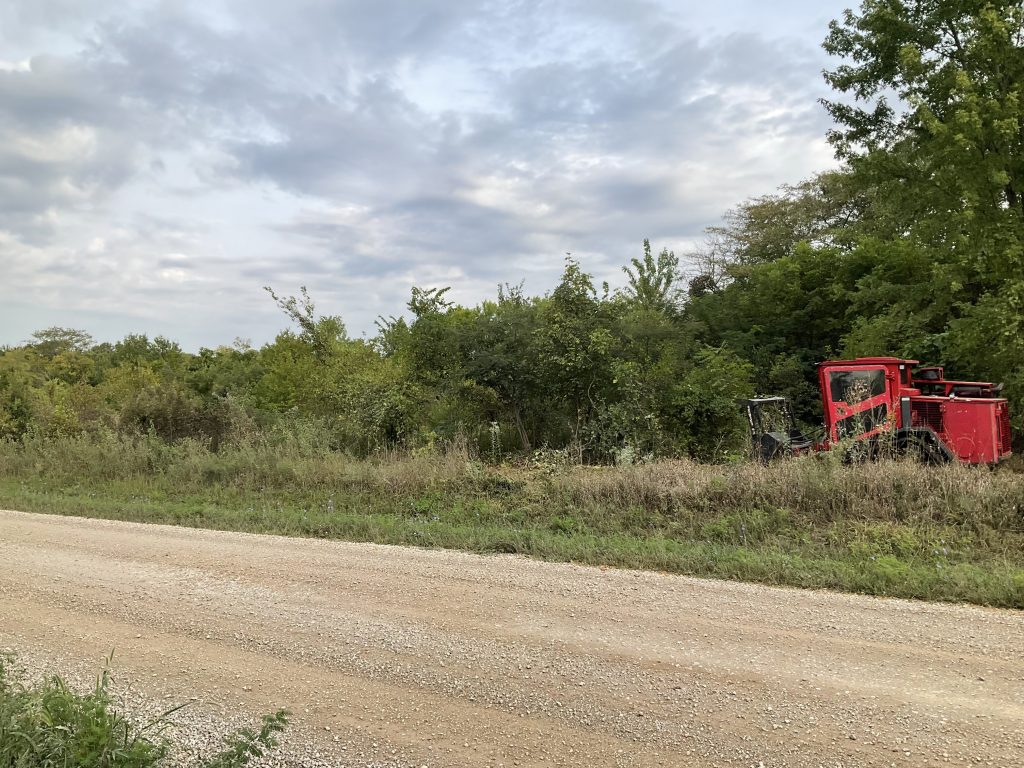 land clearing equipment shreds through brush and small trees as it clears off an overgrown field.